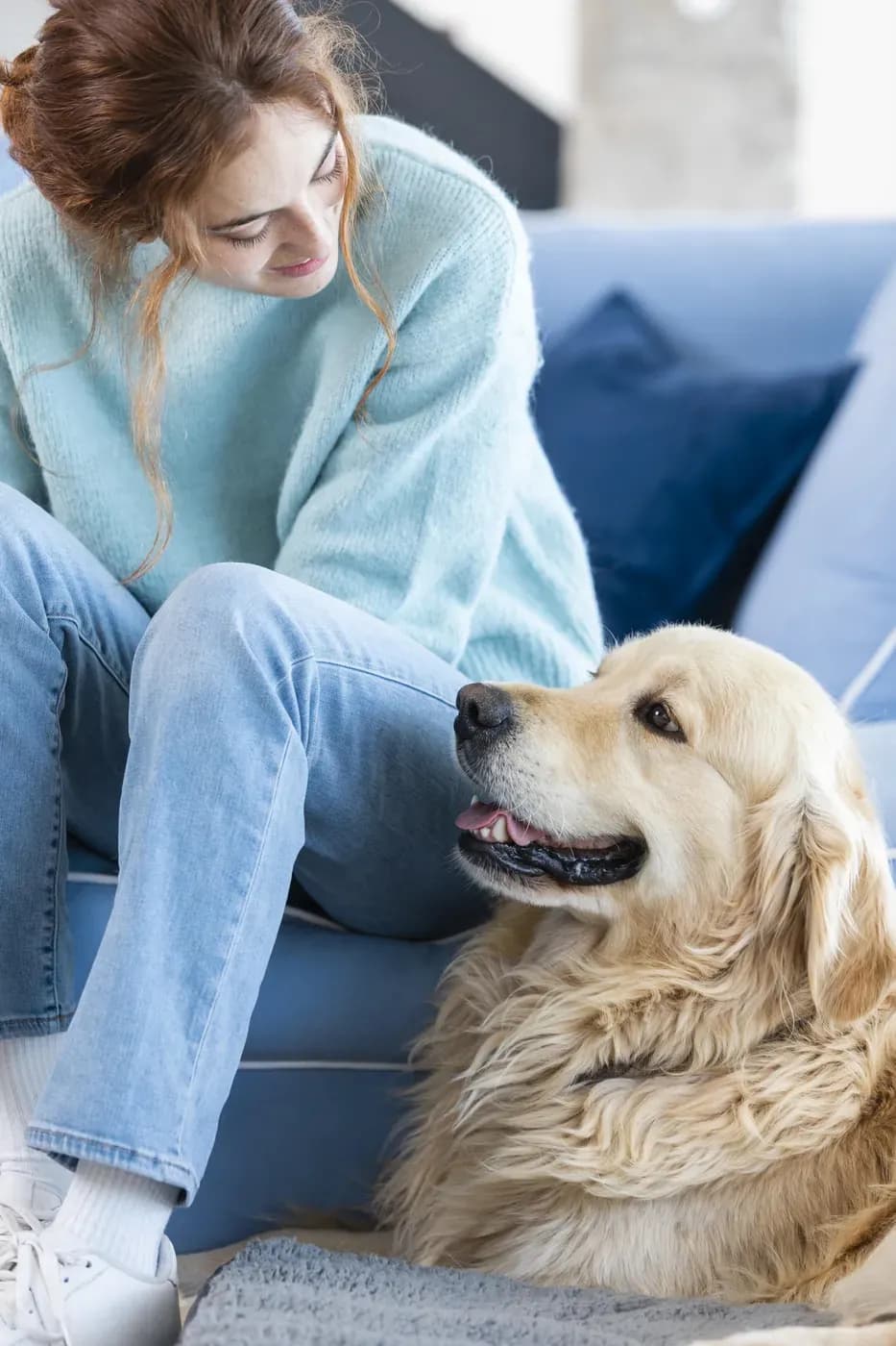 O femeie stă pe canapea lângă un golden retriever